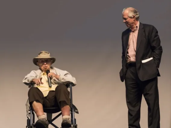 Man in wheelchair speaking into microphone on stage next to Dr. Robbins