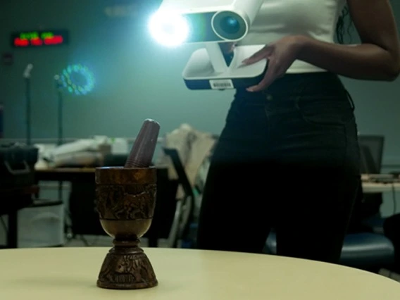 A woman holding a piece of techology standing behind a wooden artifact