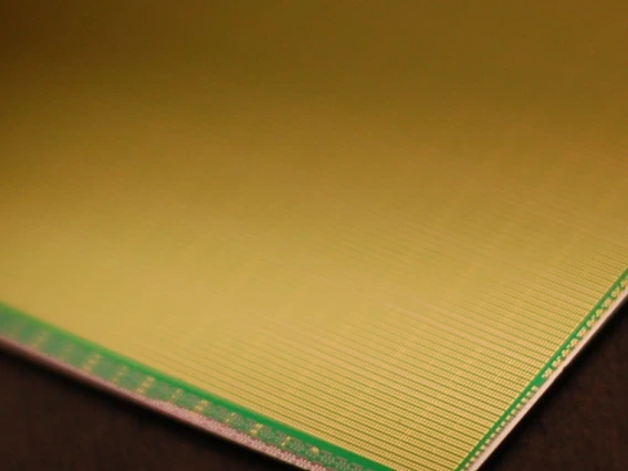 Close-up image of a microchip or electronic wafer, showcasing its intricate grid-like structure and a green border detail, likely part of a memory array or semiconductor device. The image emphasizes precision and advanced technology components.