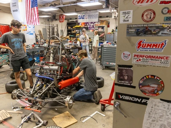 Workshop with people assembling a racing vehicle, surrounded by tools and automotive banners.