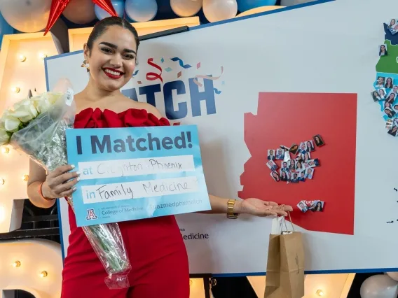 A woman in a red dress holds a sign that reads "I Matched!"